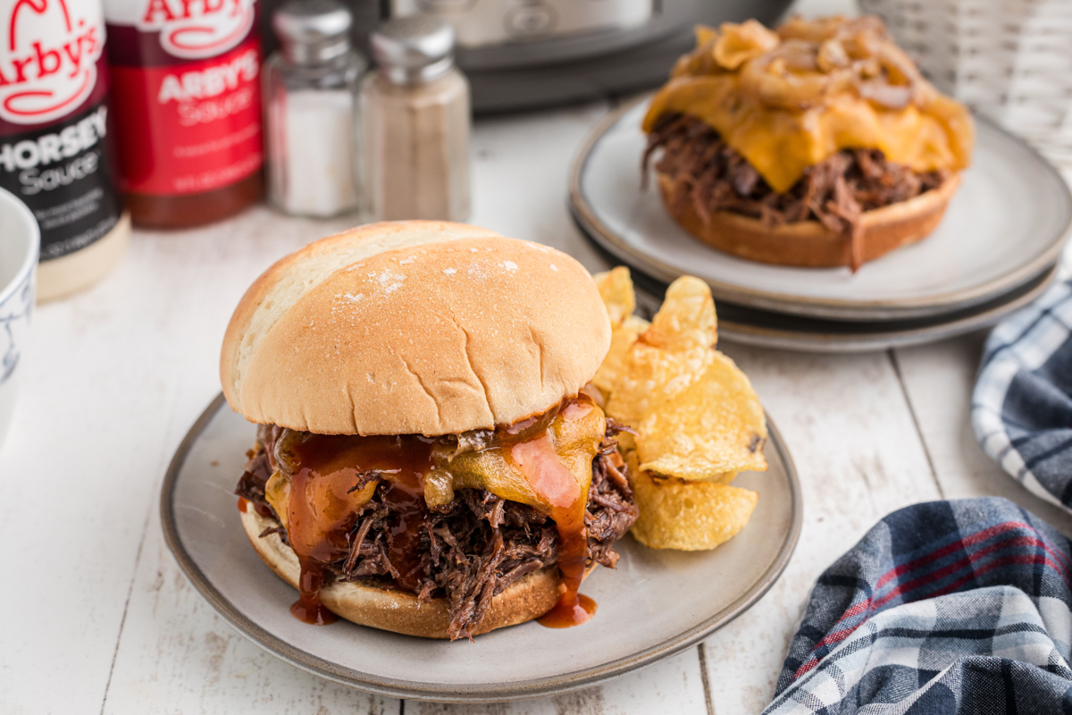 two plated slow cooker beef and cheddar sandwiches.