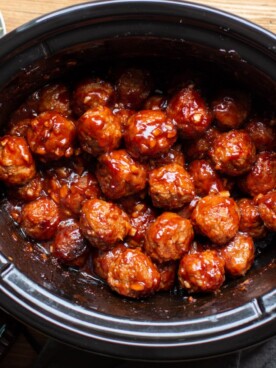meatballs in a slow cooker with bottle of barbecue sauce and toothpicks on the side.