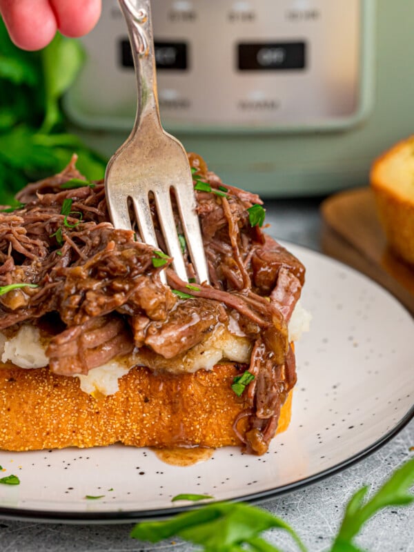 A hand holding a fork going into a piece of beef manhattan toast.