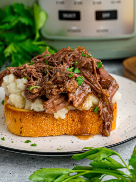 A serving of beef manhattan on a plate in front of a crockpot.