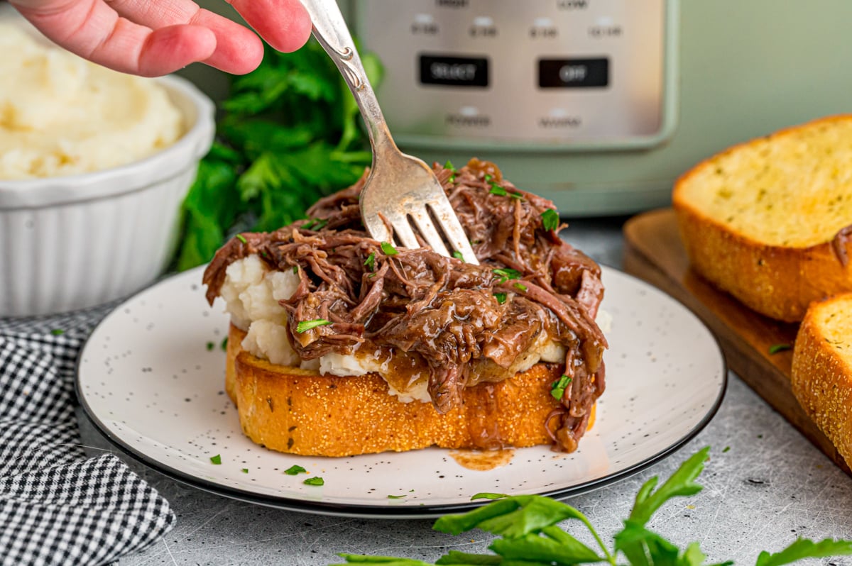 A fork cutting into a piece of beef manhattan toast.