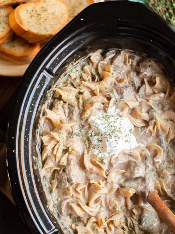 close up of stroganoff in slow cooker with dollop of sour cream.