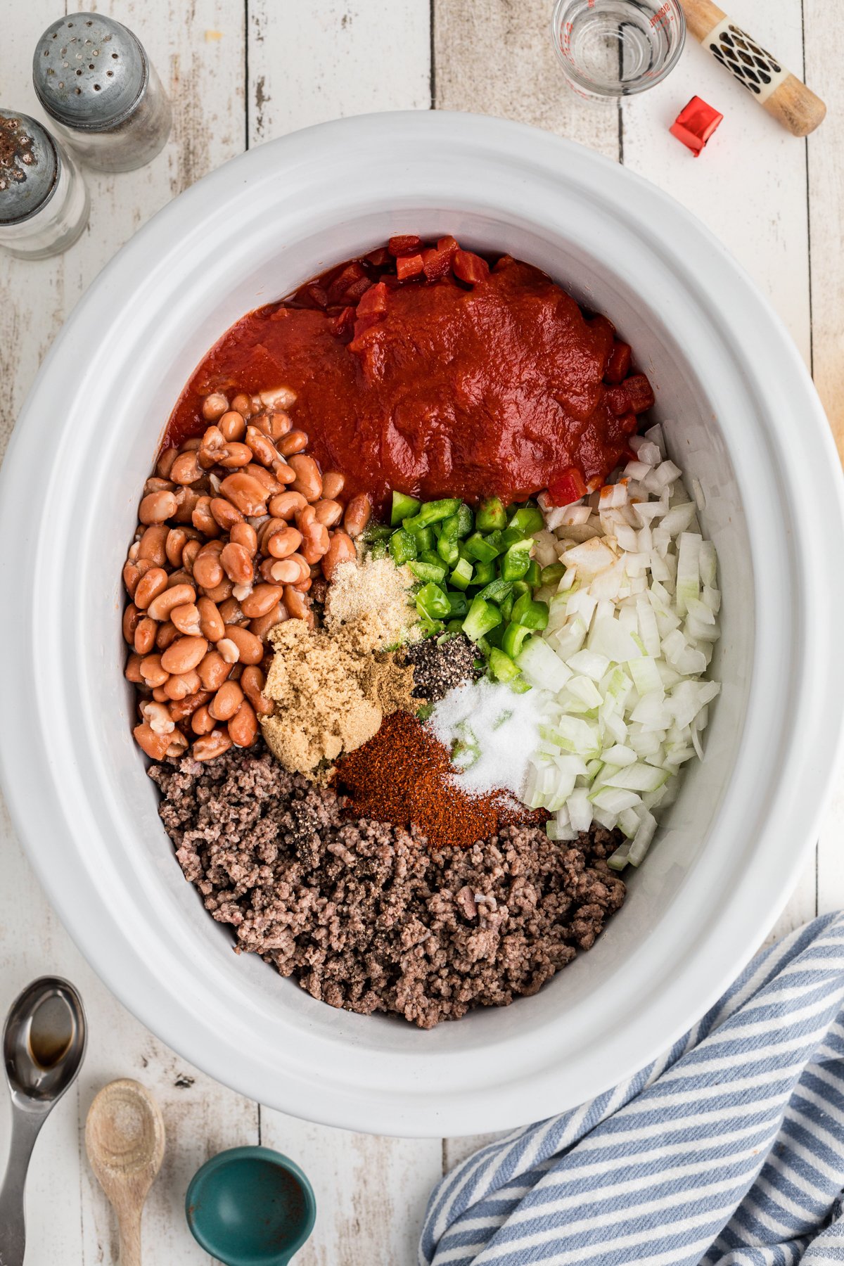 Ingredients for chili (meat, beans, veggies, seasonings and tomatoes) in a slow cooker.