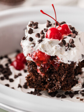 A slice of black forest cake being held up over a crockpot.