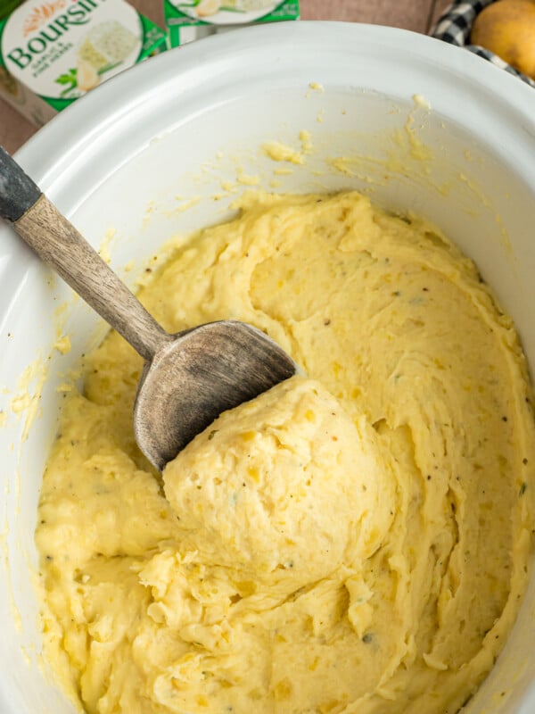 Slow cooker boursin cheese potatoes with a wooden spoon scooping some out.