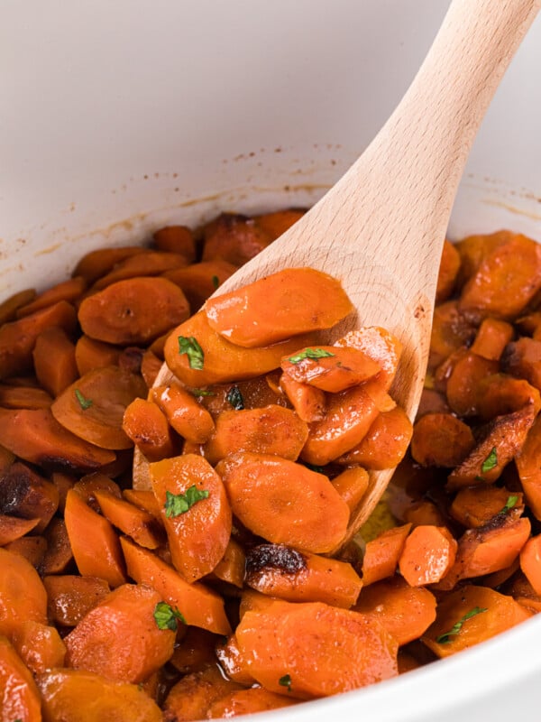 A wooden spoon holding some brown sugar carrots in a crockpot.