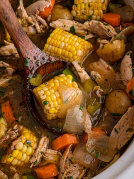 A wooden spoon grabbing some caldo de pollo from a crockpot.