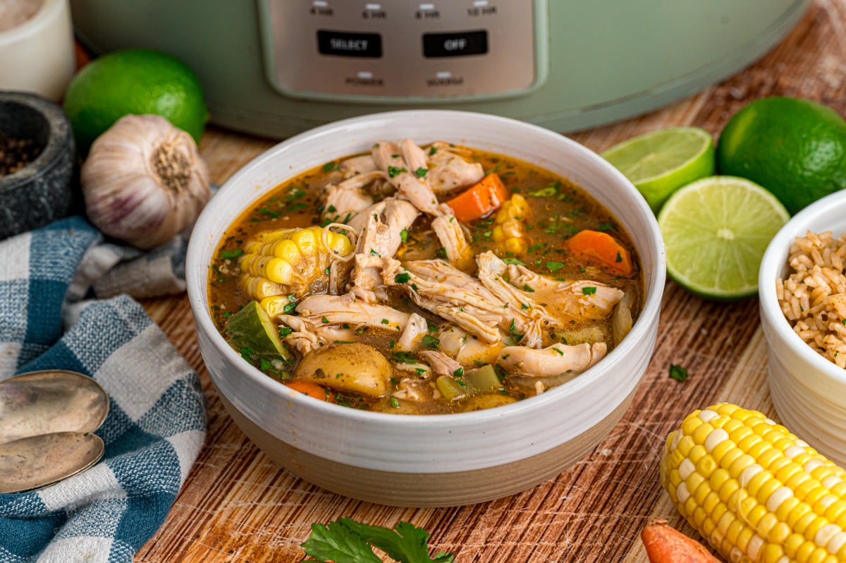A bowl of caldo de pollo in front of a crockpot.