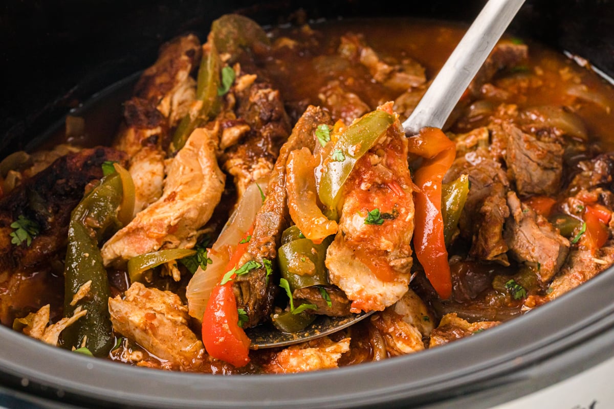 A spoon taking a scoop of fajita meat and veggies from a crockpot.