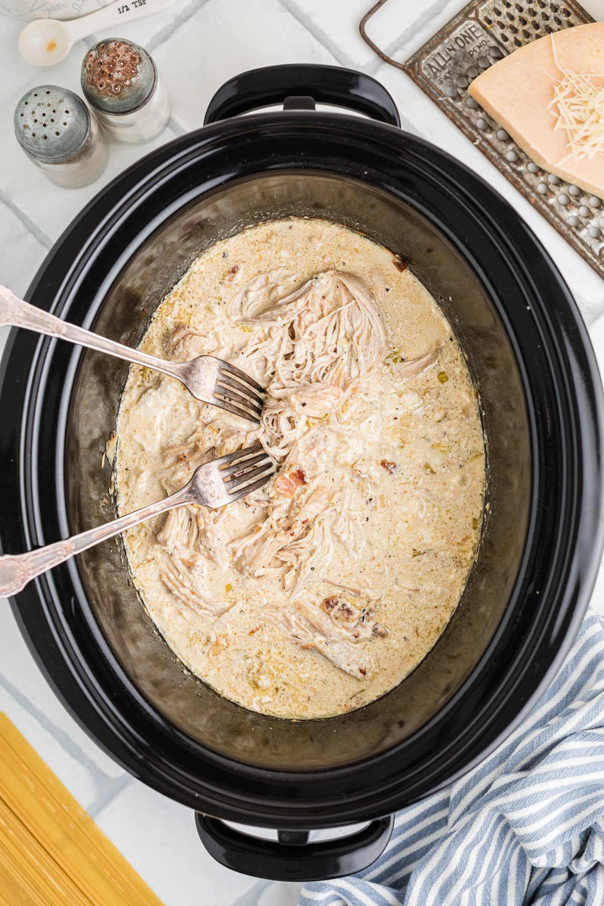 Two forks shredding chicken in a crockpot.