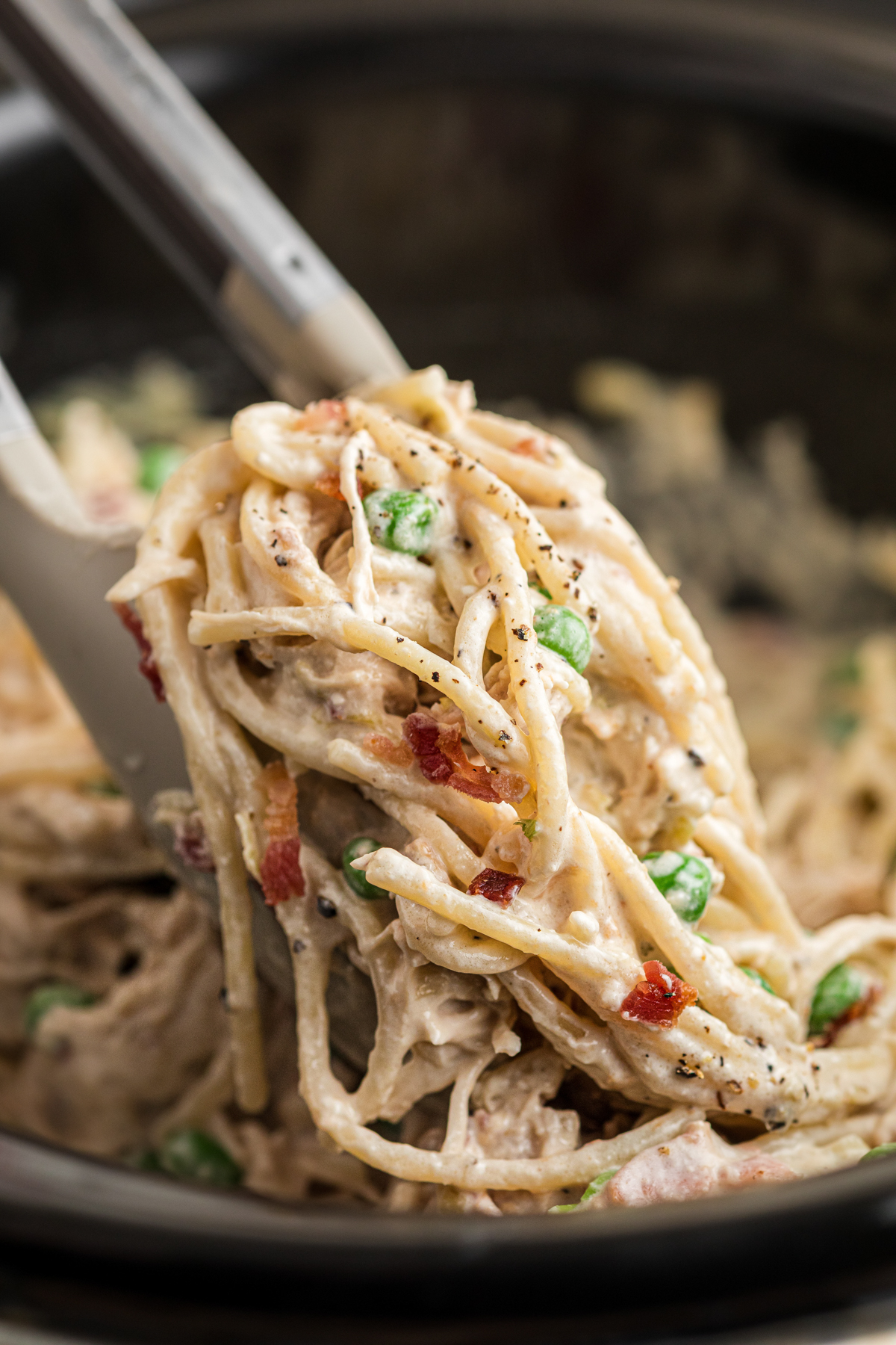 Slow cooker chicken carbonara being pulled up with tongs.