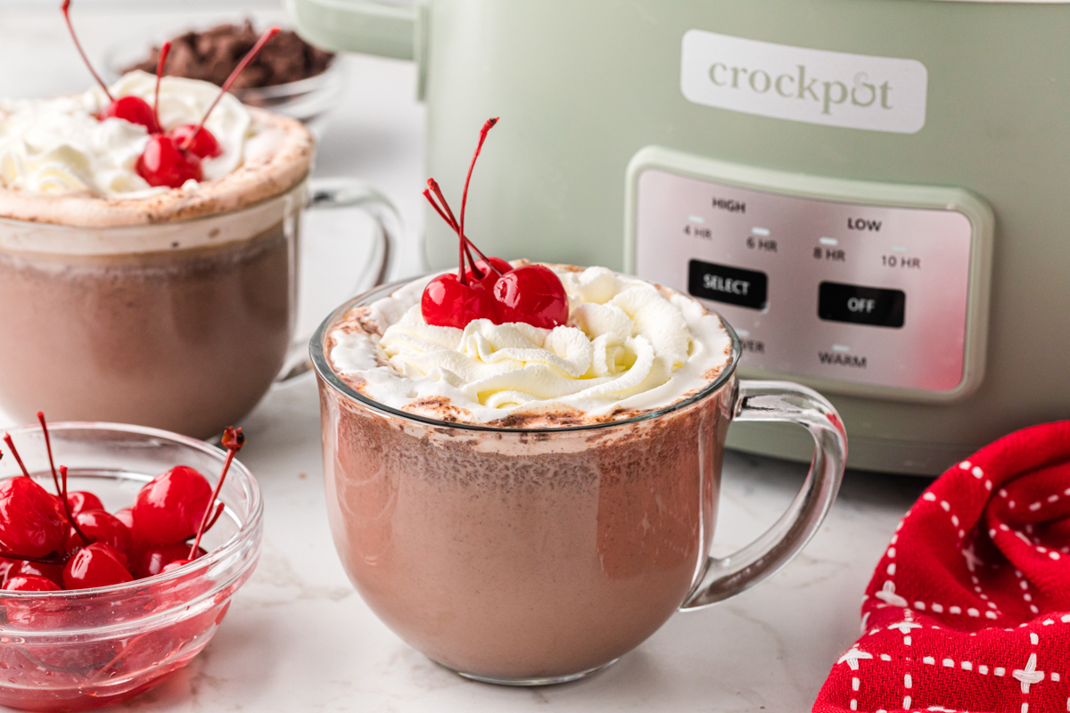 Slow cooker chocolate covered cherry hot chocolate in mugs in front of a crockpot.
