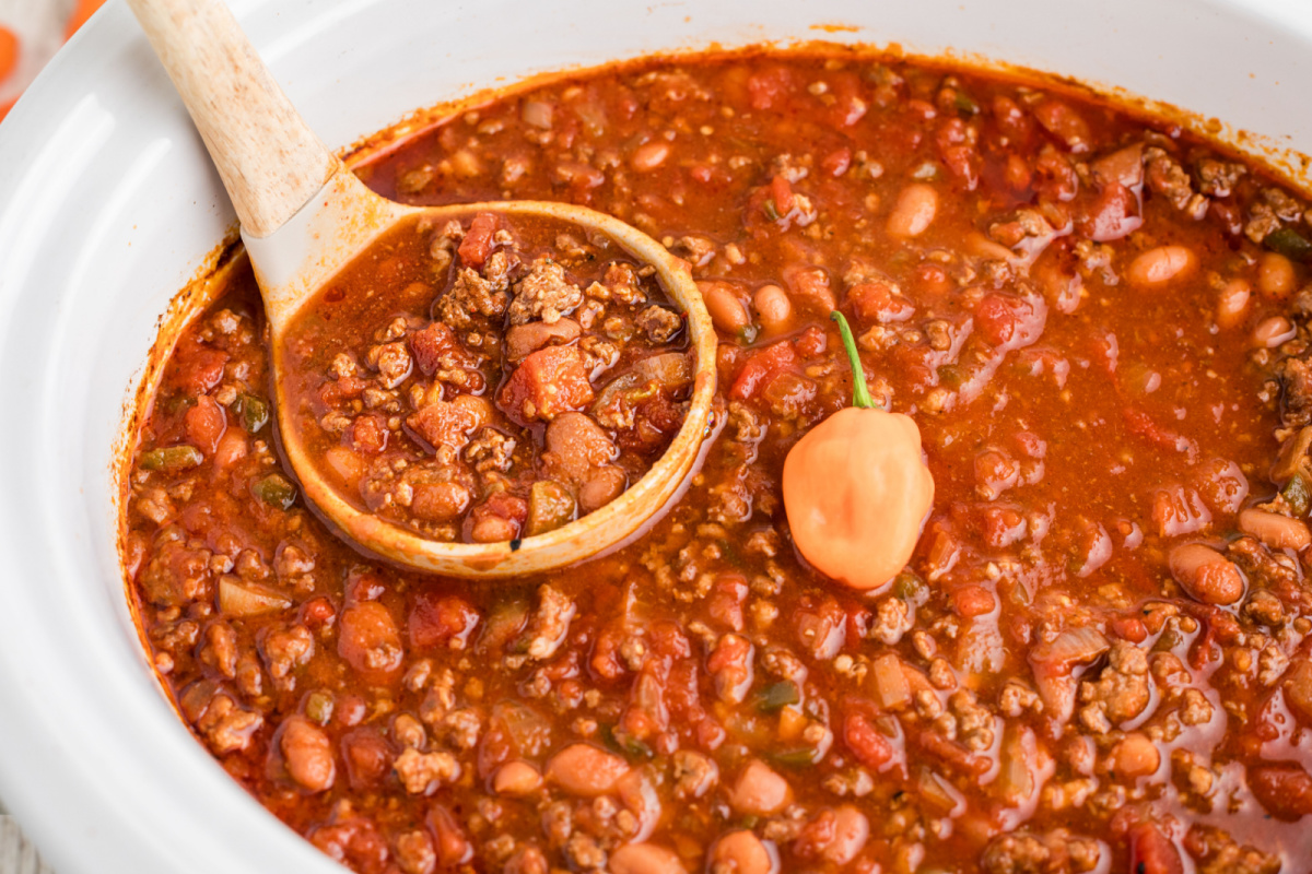 Chili in a slow cooker with a scoop and a habanero in it.