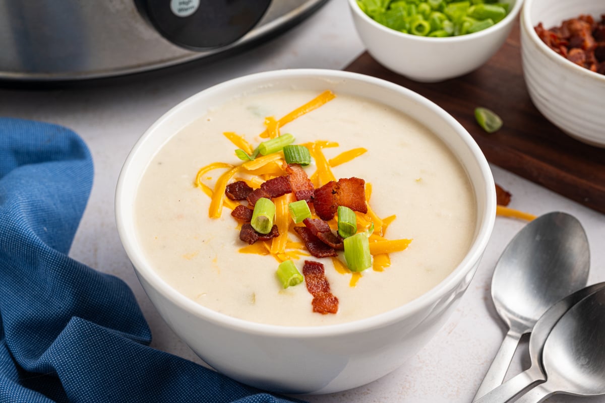 A bowl of potato soup with cheese, green onions, and bacon on top.