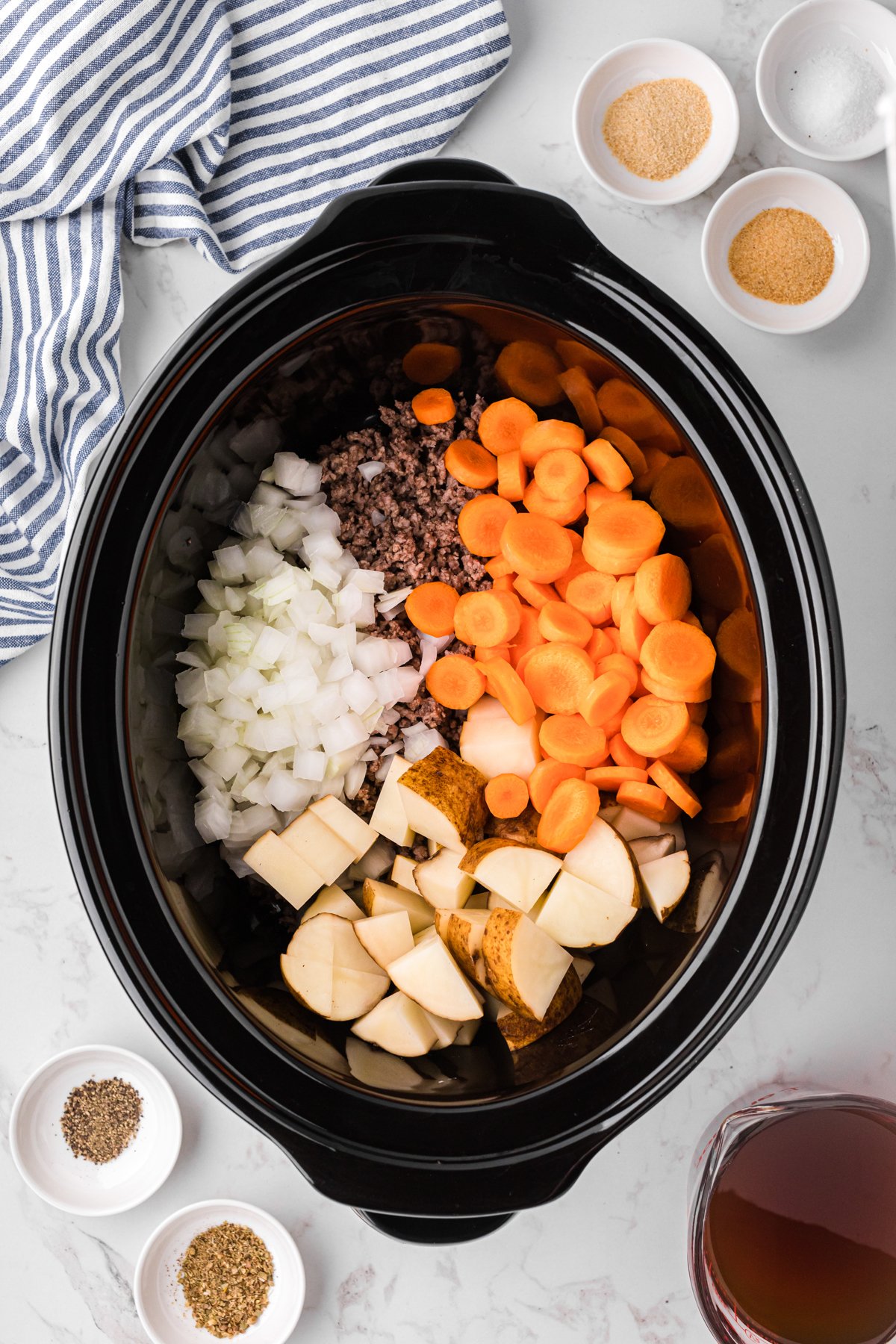Ground beef, onion, carrots, and potatoes added to a crockpot.