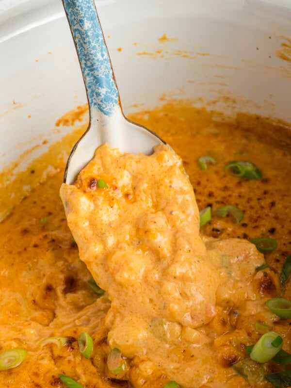 scooping hot shrimp dip out of slow cooker with a spoon.