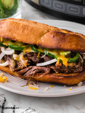 One of the slow cooker jalapeno beef sammies on a white plate in front of a crockpot.