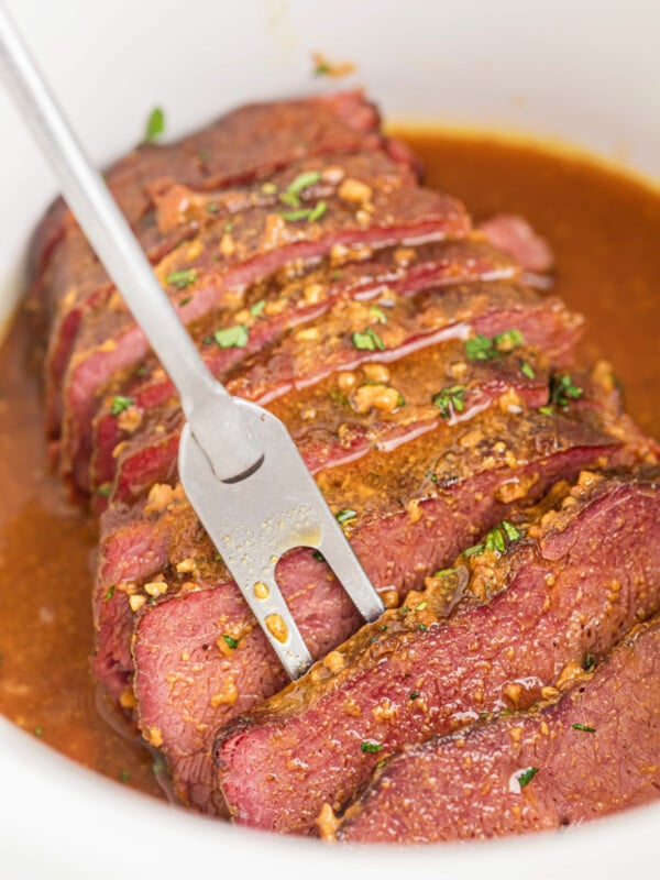 A serving fork grabbing a piece of slow cooker maple mustard corned beef.