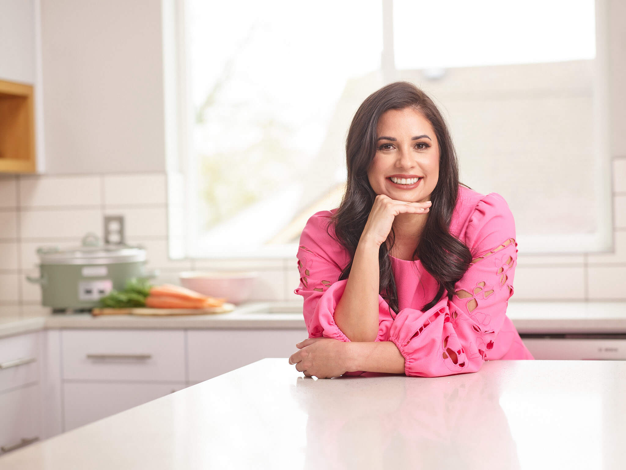 Image of sarah olson in a pink dress with her hand under her chin.