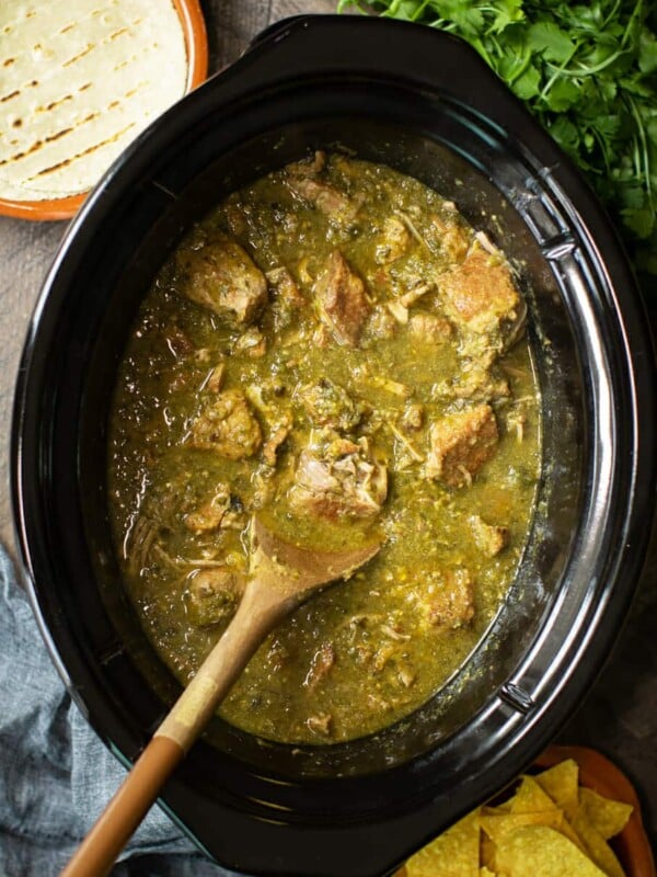 pork chile verde in slow cooker with wooden spoon in it.