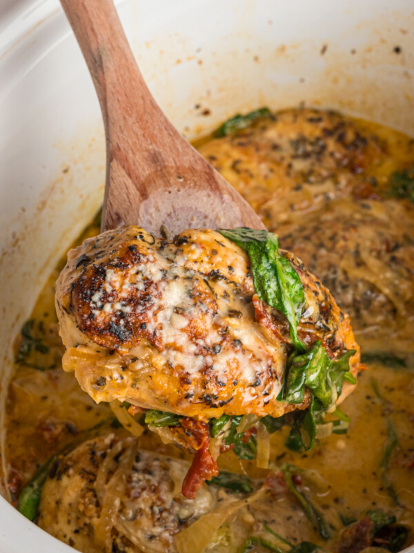 scooping a piece of tuscan chicken from a crockpot.