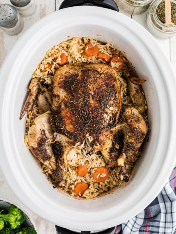 A whole chicken in a slow cooker with rice and vegetables.