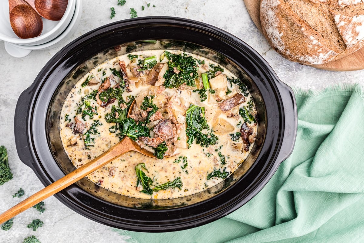 Cooked zuppa toscana in crockpot with cream and kale.